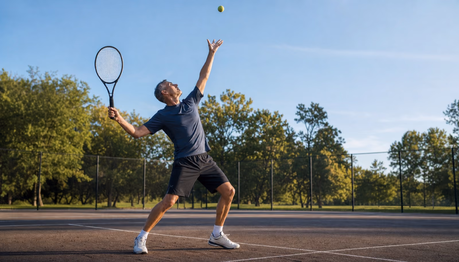 An athletic man reaches up mid-serve on a tennis court